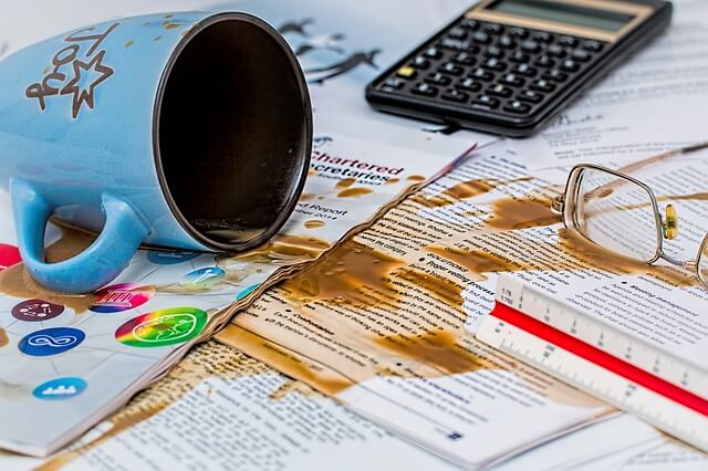 A cup of coffee tipping over a bunch of papers.